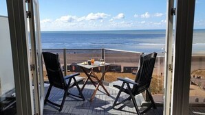 A balcony with two chairs and a table, overlooking a beach with the ocean and a clear sky. - Helmduin 5D Comfortable Holiday Residence (Egmond aan Zee)