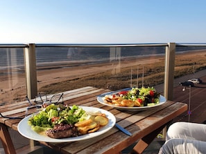 Deux assiettes de nourriture sur une table en bois, avec vue sur une plage et l’océan.
