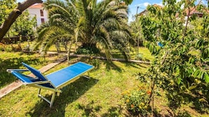 Une table de ping-pong bleue se trouve dans un espace verdoyant, agrémenté de palmiers, avec un bâtiment blanc en arrière-plan.