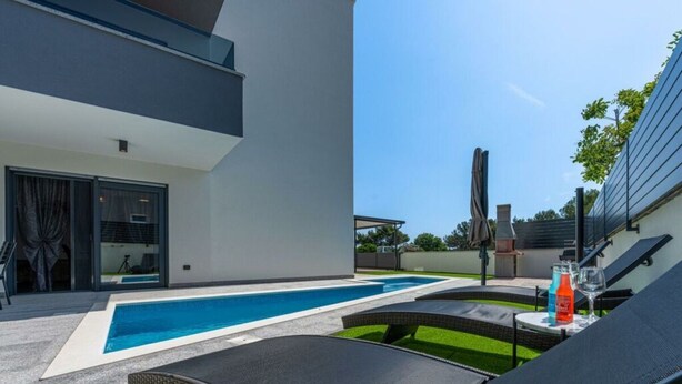 Un espace piscine extérieur moderne, doté de chaises longues et d’un barbecue.