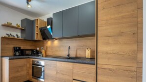 Une cuisine moderne avec des meubles en bois, un four encastré et un plan de travail noir.