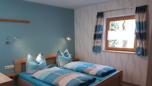 A bedroom with a single bed, a bedside table, a window with curtains, and a wall-mounted lamp. - Holiday Apartment Maurer Apartment Laber (Oberammergau)