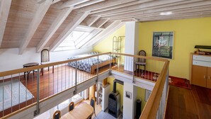 Un loft spacieux avec de hauts plafonds, des poutres apparentes, une lucarne, un lit en mezzanine, un coin repas et une cuisine équipée d’un poêle à bois.