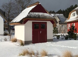 Um pequeno edifício coberto de neve, com porta vermelha e telhado de palha.