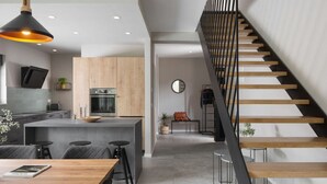 Una cocina moderna con una isla central, un comedor con mesa de madera y una escalera con barandilla negra.