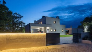 Una casa moderna de dos pisos con un coche en la entrada, rodeada de césped cuidado y árboles.