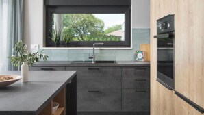 Una cocina moderna con armarios oscuros, un ventanal grande y un horno empotrado.