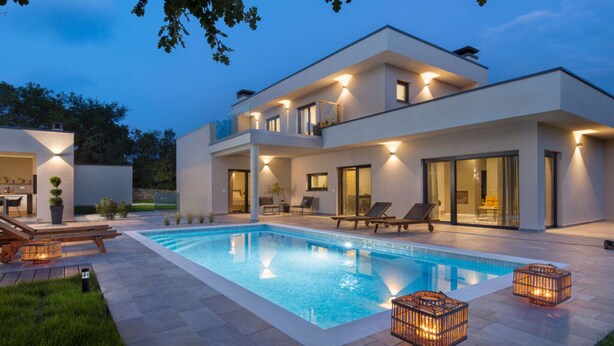 Una casa moderna de dos pisos con piscina, mobiliario exterior y un patio bien iluminado.