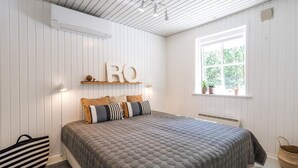 A bedroom with a bed, pillows, a bedside table, a window, and a radiator. - 4 Star Holiday Home in Norre Nebel (Norre Nebel)