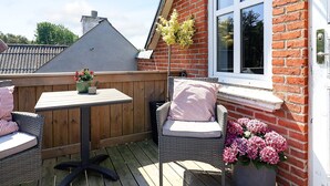 En træterrasse med et bord og stole, en murstensmur og et vindue.