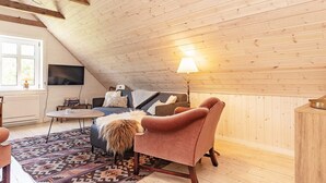 Et hyggeligt loftværelse med skråvæg, stort vindue, sofa, sofabord og lampe.