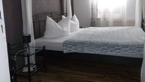A bedroom with a four-poster bed, a bedside table with a lamp, and a window with sheer curtains. - Comfort Apartment Comfortable Holiday Residence (Wernigerode)