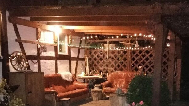 An outdoor seating area with a wooden bench, a leather chair, and a table with string lights. - Comfort Apartment Comfortable Holiday Residence (Wernigerode)