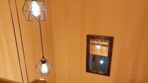 A wooden staircase with a railing, a small window with a mirror, and two hanging pendant lights. - Mari Comfortable Holiday Residence (Koserow)