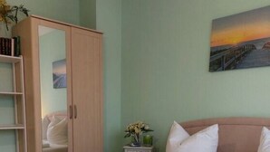A double bed with white linens and towels, a wooden wardrobe, a nightstand with a vase of flowers, and a painting of a sunset on the wall. - Mari Comfortable Holiday Residence (Koserow)