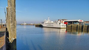 Een veerboot aangemeerd aan een steiger, met een helder uitzicht op het water en een gebouw met een rood dak op de achtergrond.