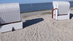 Twee rieten strandstoelen op een zandstrand met vrij uitzicht op de oceaan.