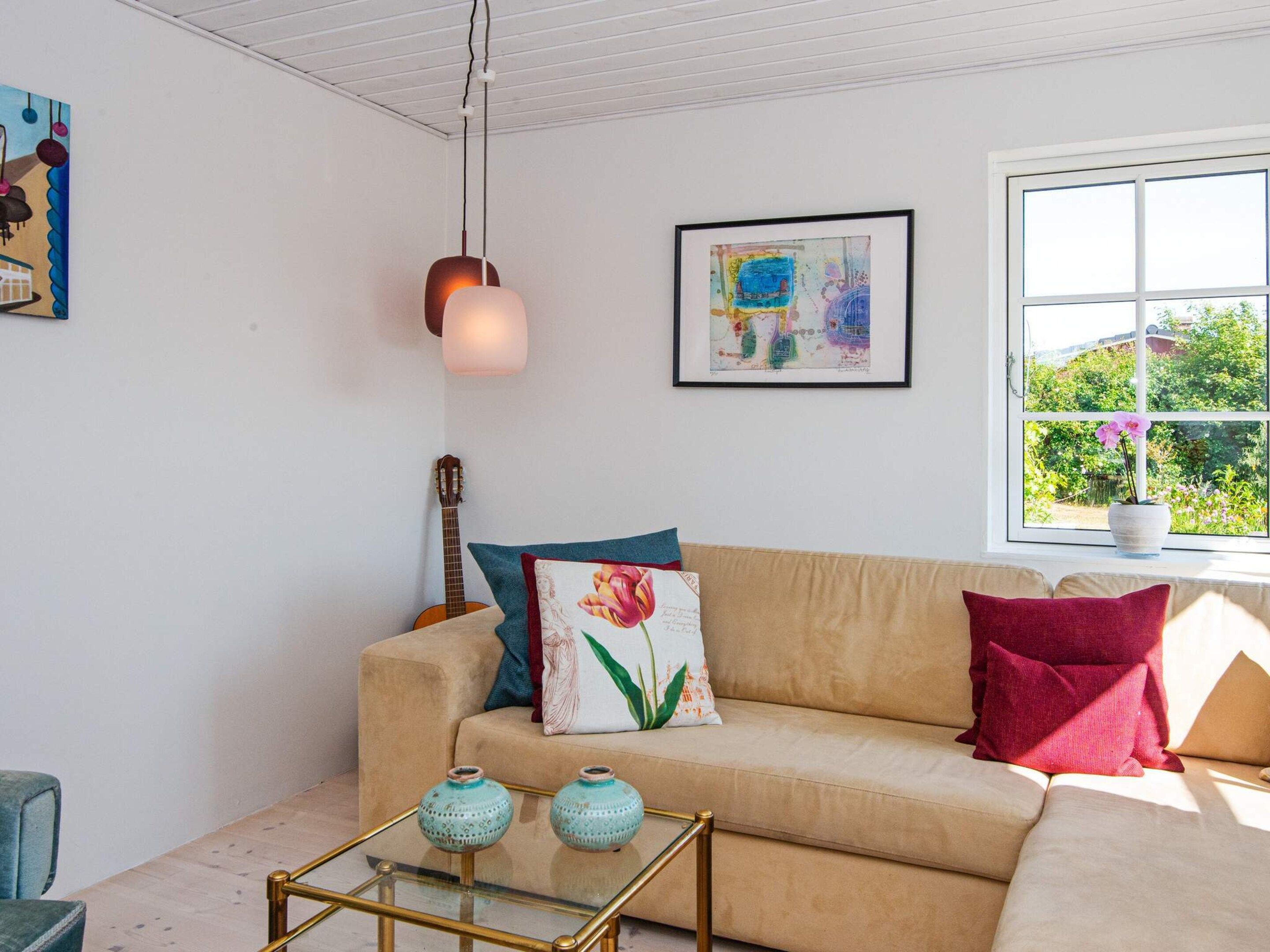 A living room with a sofa, a glass coffee table with decorative vases, a guitar, a hanging light fixture, and a framed abstract painting.