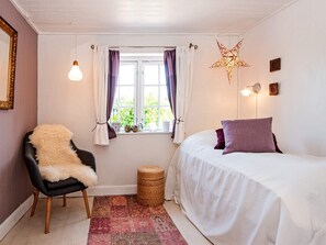 A bedroom with a bed, a chair with a fur throw, a window with curtains, a star decoration, and a small basket. - 4 Person Holiday Home in Malling (Malling)