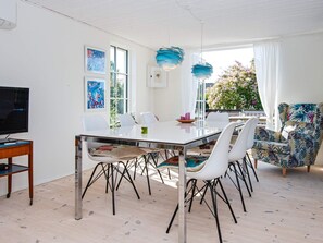 A modern dining area with a white table, black metal chairs, and a television on a wooden stand. - 4 Person Holiday Home in Malling (Malling)