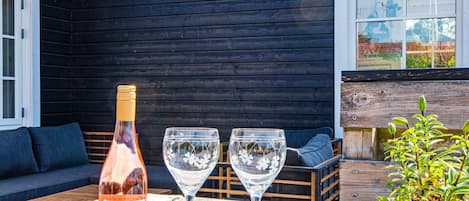 A bottle of wine, two wine glasses, a wooden bench, and a potted plant on an outdoor table.
