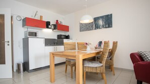 A compact kitchen with modern appliances, a dining table with wicker chairs, and a red sofa. - Apartment mit Balkon Nahe am Erlebnisberg Kappe (Winterberg)