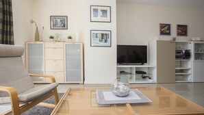 A modern living room with a sofa, a glass coffee table, a TV, and a cabinet with framed pictures. - Apartment mit Balkon Nahe am Erlebnisberg Kappe (Winterberg)