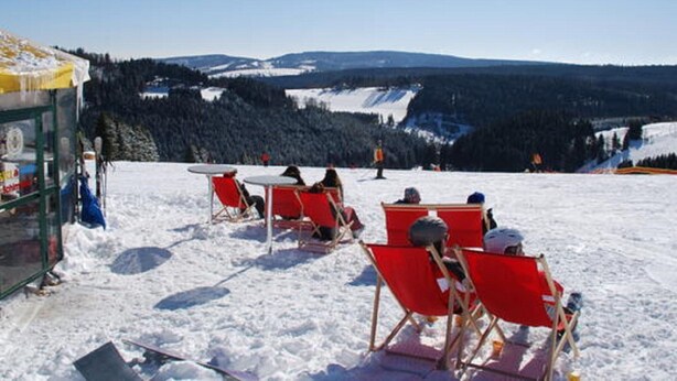 A snow-covered outdoor seating area with red chairs and tables, overlooking a mountainous landscape. - Apartment mit Balkon Nahe am Erlebnisberg Kappe (Winterberg)