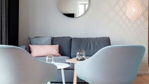 A modern living room with a grey sofa, two armchairs, a small round table, a hanging mirror, and a pendant light. - 3 in het Huis Meerloft (Norderney)