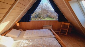 A cozy attic bedroom with two beds, a window with curtains, and a wooden ladder. - Holiday Home sea Waves (Brodersby)