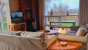 A cozy living room with a sofa, a wooden coffee table, a TV, and a fireplace. - Holiday Home sea Waves (Brodersby)