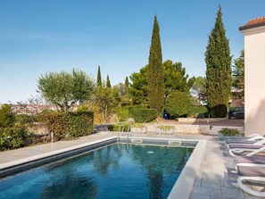 Une piscine rectangulaire bordée de pierres, entourée de chaises longues et d’un muret en pierre.