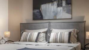 A neatly made bed with striped pillows and a dark throw, a wall clock, and a lamp on a bedside table. - Villa Rosy Comfortable Holiday Residence (Rovinj)