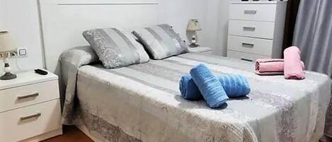 A bedroom with a bed, pillows, a nightstand, a dresser, and a vase with flowers.