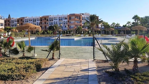 Een resort met een zwembad, palmbomen en een rij meerhoogbouw met balkons.