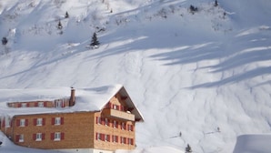 Ein Chalet-ähnliches Gebäude mit zahlreichen Fenstern und einem geneigten Dach, umgeben von verschneiter Landschaft.