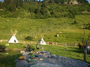 Un paysage rural avec deux tipis blancs, une clôture en bois et un petit étang.