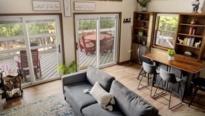 A cozy living room with a gray sofa, a wooden dining table with chairs, and a sliding glass door leading to an outdoor patio.