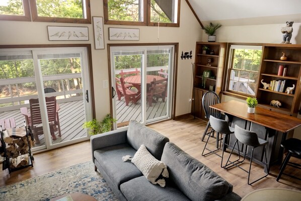 A cozy living room with a gray sofa, a wooden dining table with chairs, and a sliding glass door leading to an outdoor patio.