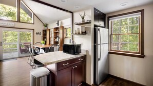 A kitchen with a large window, wooden cabinets, a refrigerator, and a microwave on the counter.