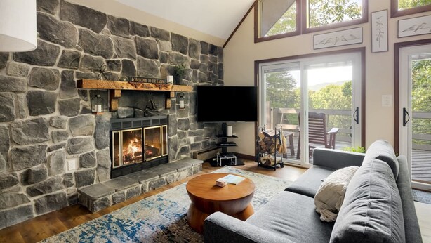 A cozy living room with a stone fireplace, a flat-screen TV, and a comfortable gray sofa.