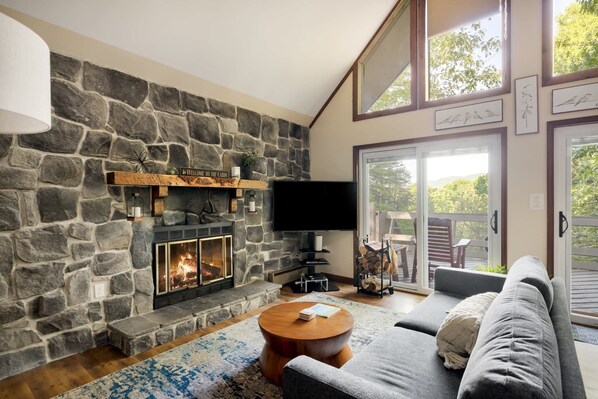 A cozy living room with a stone fireplace, a flat-screen TV, and a comfortable gray sofa.