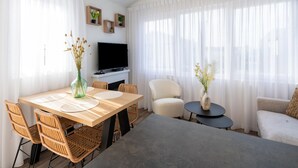 A modern living room with a wooden dining table, wicker chairs, a flat-screen TV, and a sofa. - Chalet in Middelkerke Near the Beach (Middelkerke)