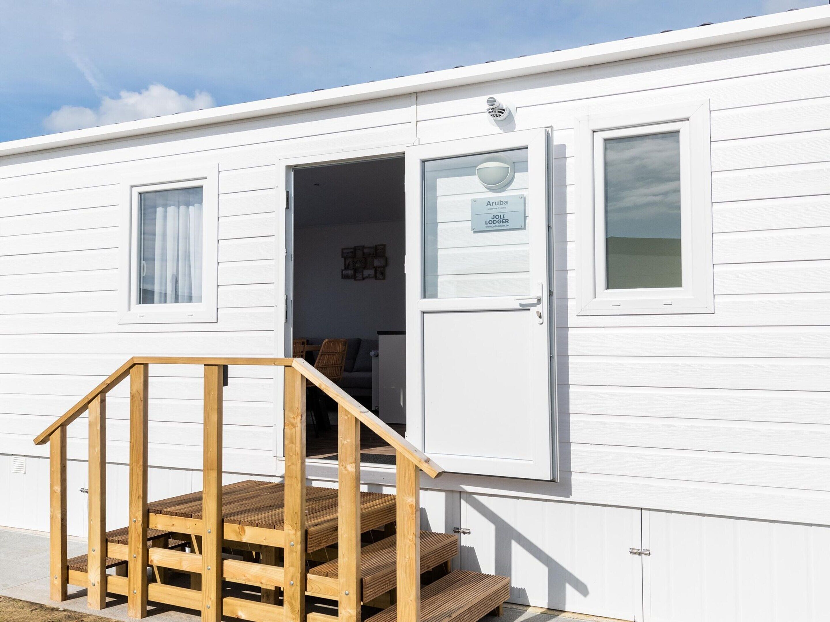 A white mobile home with a wooden staircase leading to a door labeled "Aruba Joli Lodger."