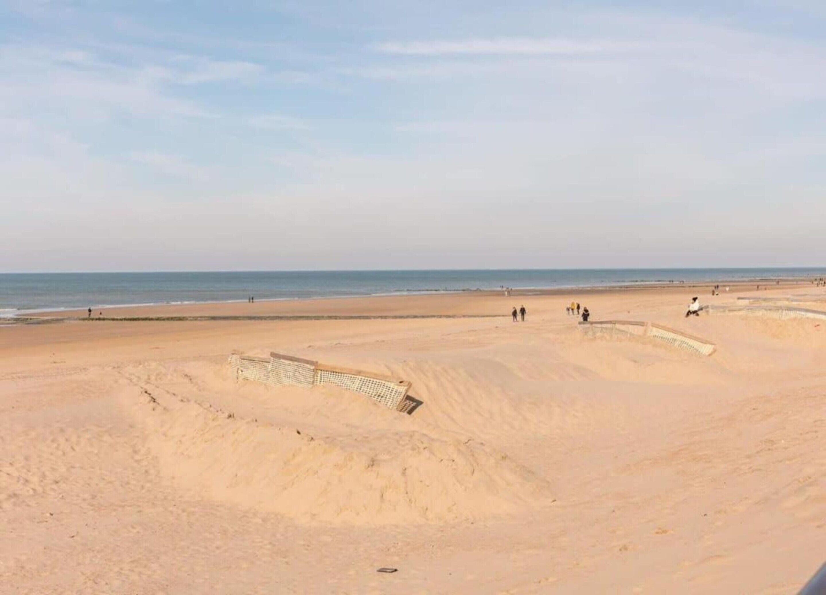 A sandy beach with a few people and a structure that appears to be a lifeguard tower.