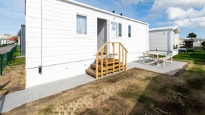 A white mobile home with a wooden staircase leading to the entrance, a small porch, and a paved area with a bench. - Chalet in Middelkerke Near the Beach (Middelkerke)