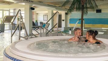 Et område med jacuzzi, palmetræ, liggestole og flisetæppe.