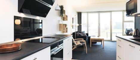 Una cocina moderna con electrodomésticos integrados, una zona de comedor con mesa y sillas, y ventanas amplias que dejan entrar luz natural.