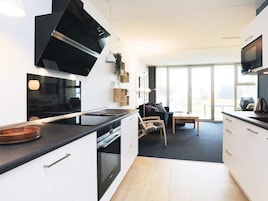 Una cocina moderna con electrodomésticos integrados, una zona de comedor con mesa y sillas, y ventanas amplias que dejan entrar luz natural.