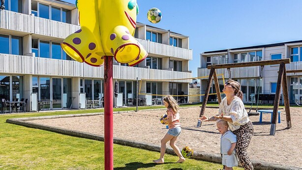 A playground with a yellow climbing structure, a volleyball net, and a swing set. - 4 Person Holiday Park Home in Blokhus (Blokhus)